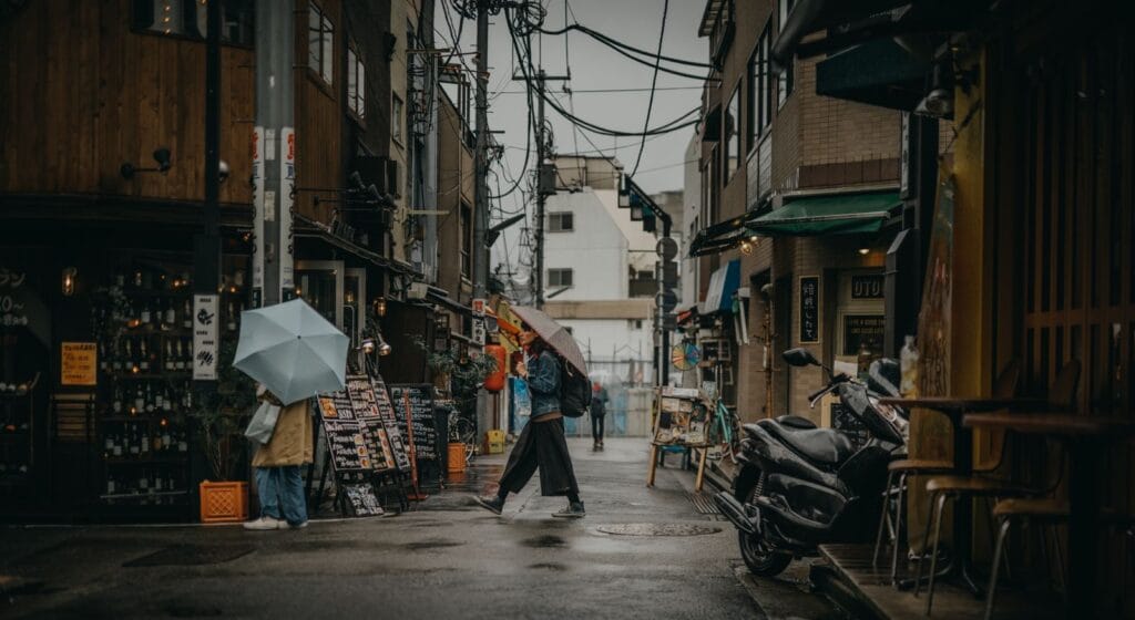 Pedestrians with umbrellas walking through a rain-soaked city street during Korea's rainy season